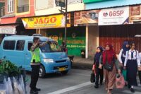 Personel Polsek Bumiayu membantu pelajar dan warga menyeberang jalan pada jam sibuk.